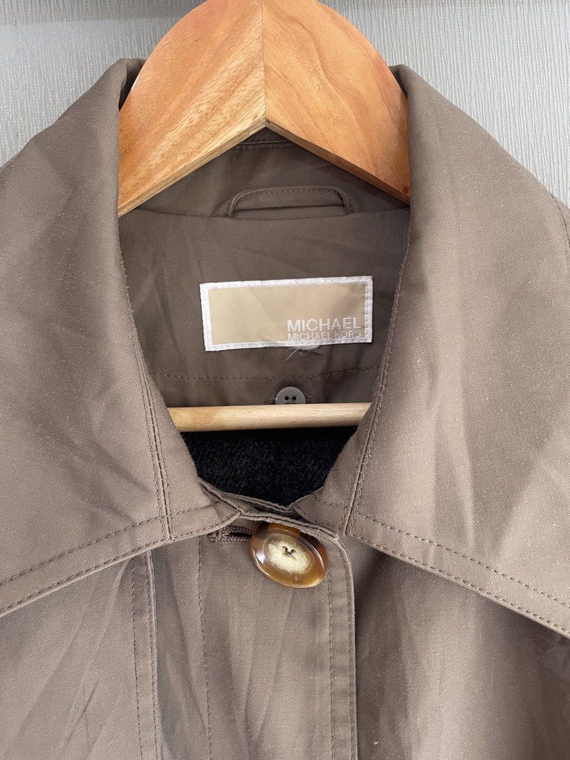 Michael Kors Brown Trench Coat (Category: Coats, Jackets and Outerwear) located in Mataasnakahoy. Submitted by zero4thrift (Listing ID 1468559482, Image 3). Description: - Brand: Michael Kors - Color: Brown - Style: Mid-length trench coat, great for cooler weather - Closure: Front tortoise-shell buttons - Details: Classic collar, shoulder epaulets, and cuff straps - Belt: Matching waist belt with a dark buckle included Actual size - 21” width - 3