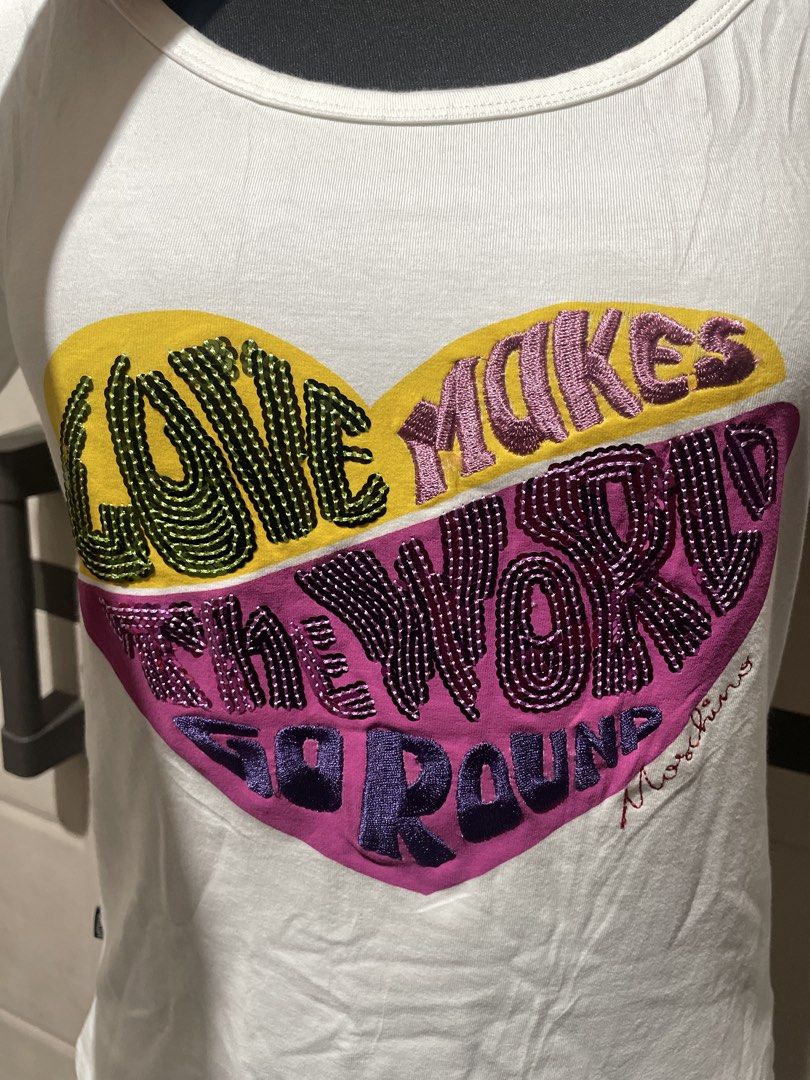 Moschino Jeans Graphic Tee (Category: Shirts) located in Roxas City. Submitted by budgetfindsroxasph (Listing ID 1468626493, Image 2). Description: Heart graphic with typography reading “Love Makes The World Go Round” accompanied by a embroidered Moschino signature at the bottom right of the heart. Brand / Line: Moschino Jeans (Made in Italy) Item Type: Women’s Scoop Neck Short-Sleeve Graphic T-Shirt Color: White / Off-White 📩📩📩.
