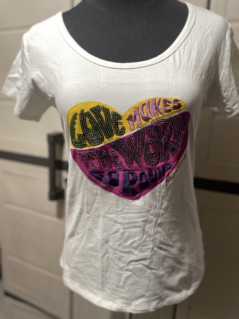 Moschino Jeans Graphic Tee (Category: Shirts) located in Roxas City. Submitted by budgetfindsroxasph (Listing ID 1468626493, Image 1). Description: Heart graphic with typography reading “Love Makes The World Go Round” accompanied by a embroidered Moschino signature at the bottom right of the heart. Brand / Line: Moschino Jeans (Made in Italy) Item Type: Women’s Scoop Neck Short-Sleeve Graphic T-Shirt Color: White / Off-White 📩📩📩.