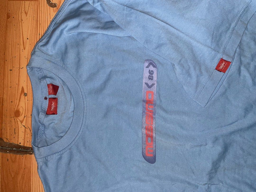 Mossimo 86 Vintage Light Blue T-Shirt (Category: Tshirts & Polo Shirts ) located in Manila. Submitted by joshua_guimeroy. (Listing ID 1468524537, Image 3). Description: - Brand: Mossimo 86 - Color: Light blue - Design: Logo graphic across the chest and matching larger print near the back collar - Details: Short sleeves with a small red brand tag on the left sleeve, standard crew neck fit - Flaw: Small stain visible on the lower back area - Condit