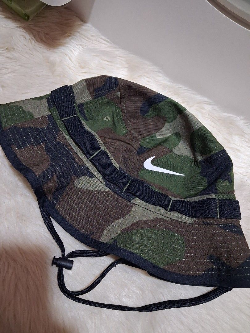 Nike Camouflage Bucket Hat with Drawstring (Category: Caps & Hats) located in Manila. Submitted by jiejieph (Listing ID 1468707838, Image 1). Description: - Brand: Nike - Style: Camouflage bucket hat - Size: Adult Unisex M/L - Color: Green, brown, and black camo pattern - Details: White embroidered Nike swoosh logo on the front - Features: Adjustable black drawstring cord with toggle and durable crown strap loops - Condition: Brand new with origi