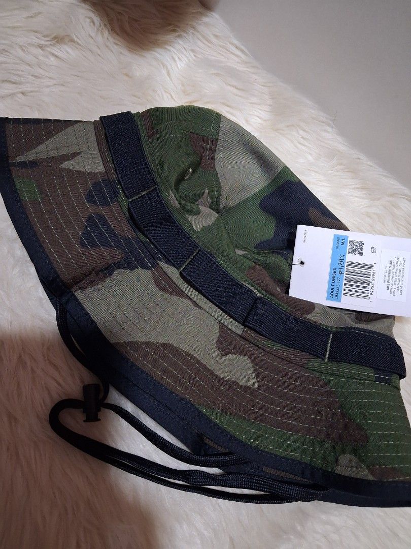 Nike Camouflage Bucket Hat with Drawstring (Category: Caps & Hats) located in Manila. Submitted by jiejieph (Listing ID 1468707838, Image 2). Description: - Brand: Nike - Style: Camouflage bucket hat - Size: Adult Unisex M/L - Color: Green, brown, and black camo pattern - Details: White embroidered Nike swoosh logo on the front - Features: Adjustable black drawstring cord with toggle and durable crown strap loops - Condition: Brand new with origi