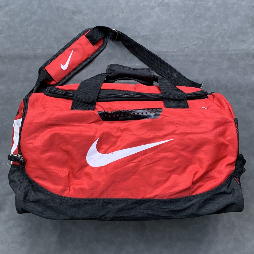 Nike Red and Black Gym Duffel Bag (Category: Backpacks) located in Manila. Submitted by 4114thriftedloots (Listing ID 1468626749, Image 1). Description: Bright red and black Nike duffel bag featuring a large white swoosh and bold logo. Includes dual carry handles, an adjustable padded shoulder strap, and a spacious zippered main compartment. Perfect for the gym, sports, or weekend getaways..