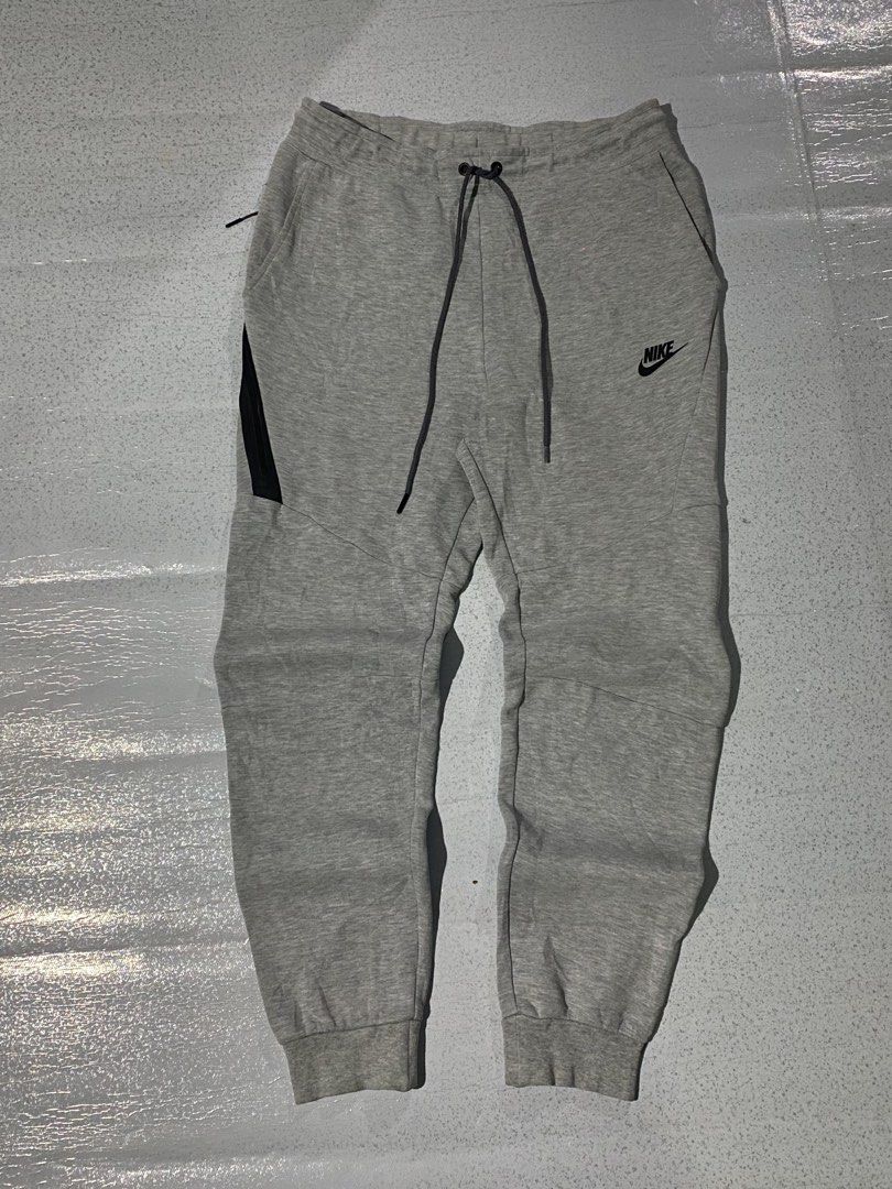 Nike Tech Fleece Joggers Grey (Category: Joggers) located in Manila. Submitted by jeproxthrift (Listing ID 1468626085, Image 1). Description: - Brand: Nike - Color: Grey with black accents - Material: Soft fleece fabric blend - Pockets: Includes a secure zipper pocket on the right leg - Waist: Adjustable drawstring with dark grey cords - Cuffs: Ribbed at the ankles - Branding: Classic embroidered Nike logo on the left thigh.