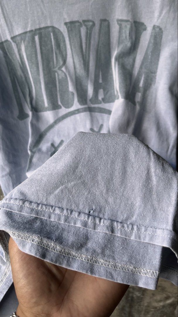 Nirvana Smiley Face Graphic Tee Acid Wash (Category: Tshirts & Polo Shirts ) located in Cabuyao City. Submitted by bulandos (Listing ID 1468636957, Image 3). Description: - Brand: Nirvana - Design: Classic smiley face print - Color/Style: Acid wash faded grey-blue - Size: Medium - Material: 100% cotton, tagless neck label - Condition: Pre-loved with one tiny hole near the bottom hem (shown in close-up photo).