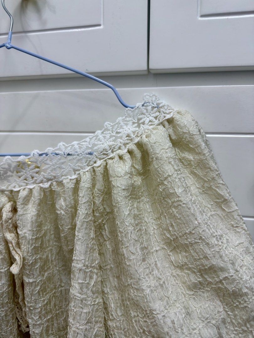 Off-shoulder cream textured blouse with lace trim (Category: Blouses) located in Manila. Submitted by chi.declutter (Listing ID 1468525594, Image 2). Description: - Color: Cream - Style: Off-shoulder top with puffy half sleeves - Details: Textured crinkle fabric, white floral lace trim, and center front tie with lace ribbon - Fit: Loose and breezy - Versatility: Easy to dress up with a skirt or keep casual with denim - Condition: Brand new / Exce