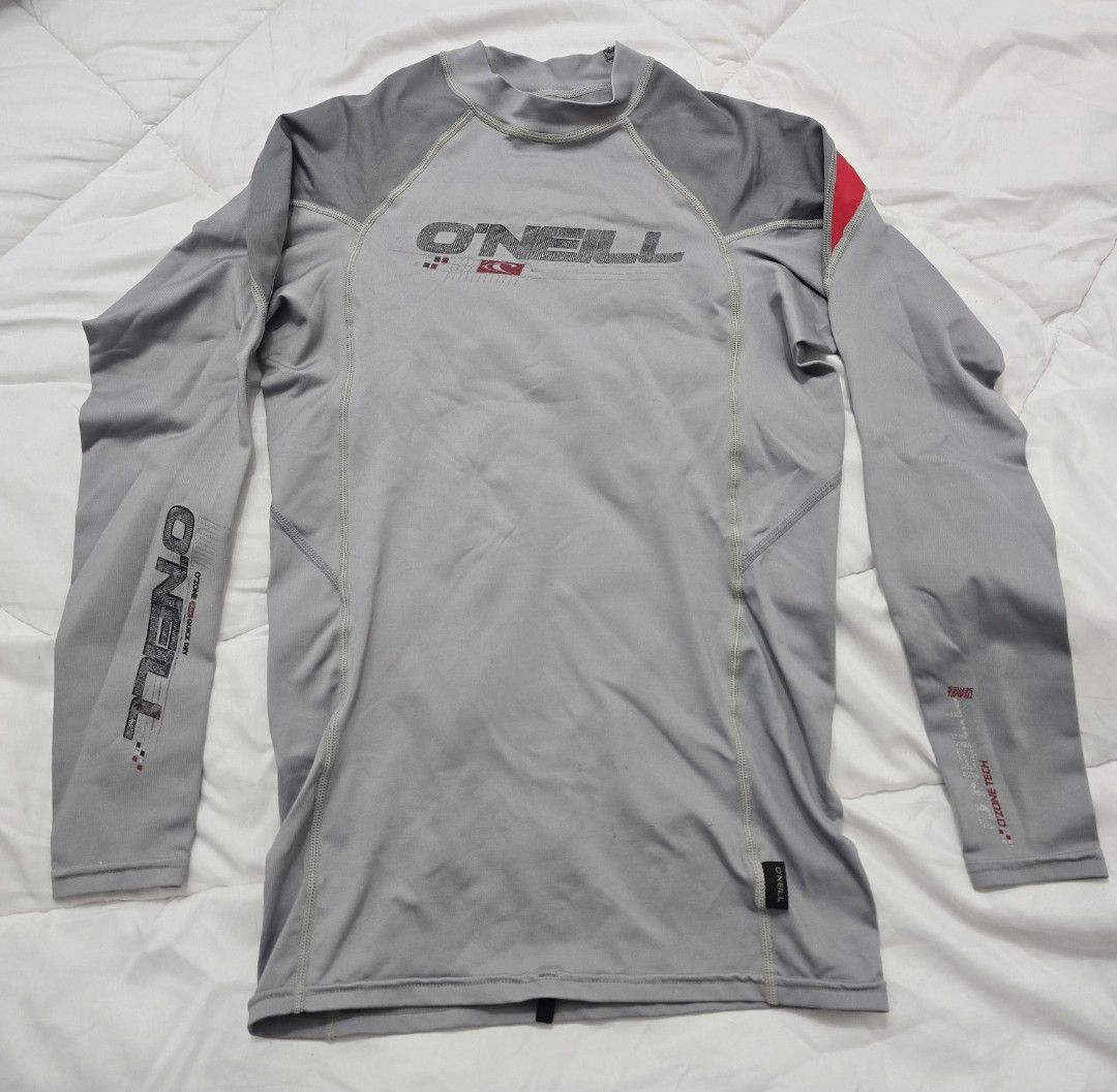 O'Neill Ozone Tech Long Sleeve Rash Guard Grey Red (Category: Water Sports) located in San Juan City. Submitted by YardSaleSanJuan (Listing ID 1468711751, Image 3). Description: - Brand: O'Neill (Ozone Tech Travel Series) - Color: Grey with red shoulder accents - Design: Long sleeves with arm branding - Special Feature: Back zipper pocket for phone or small essentials; hole for wired earphones, tie down at the back to keep it from running up your