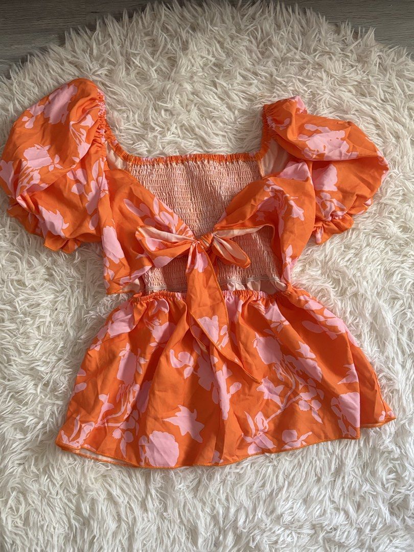 Orange Floral Puff Sleeve Tie Back Top (Category: Blouses) located in Quezon City. Submitted by lovedbysloane (Listing ID 1468596104, Image 1). Description: - Color: Bright orange with all-over pink floral print - Neckline: Square neck with a smocked back panel for a comfortable fit - Sleeves: Short puff sleeves with elastic cuffs - Details: Cute back cutout with a matching fabric tie and a flared peplum hem - Fabric: Lightweight and breathable, 
