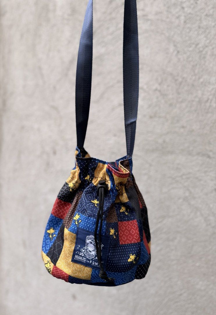 PEANUTS for FDMTL Tokyo Japan Patchwork Drawstring Bag (Category: Shoulder Bags) located in Baguio. Submitted by aalkharys (Listing ID 1468676163, Image 1). Description: - Authentic PEANUTS x FDMTL Tokyo collaboration - Eye-catching blue, yellow, and red patchwork design - Features iconic Snoopy and Woodstock graphics - Secure drawstring closure with an adjustable toggle - Dark blue shoulder strap and matching interior lining - Branded woven patc