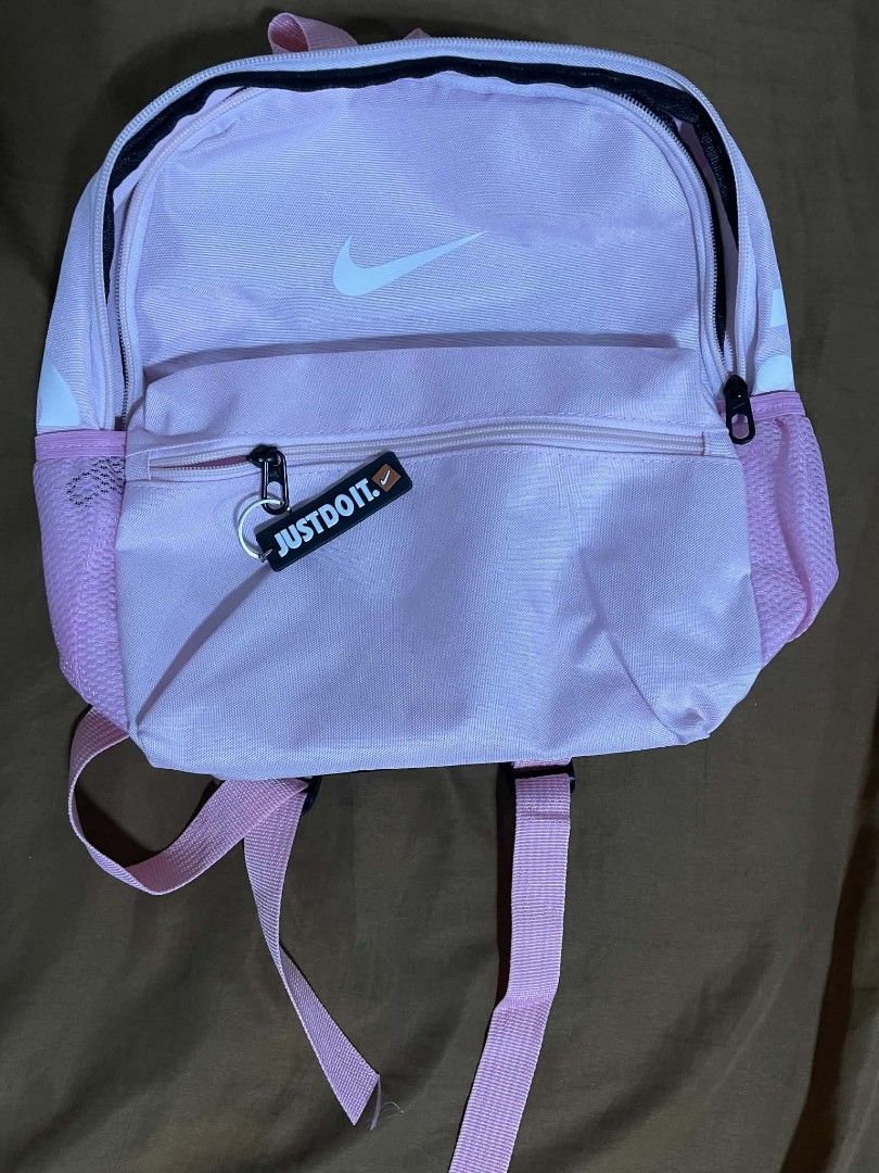 Pink Nike Backpack With Just Do It Keychain (Category: Backpacks) located in Iloilo. Submitted by lovedbymyl (Listing ID 1468601256, Image 1). Description: Nike Brasilia Mini Backpack – Pink Pretty in pink! 🎀— Light pink with a white swoosh logo • Almost brand new— Only opened, with the tag already cut (bought last week) • Cute, compact, and perfect for everyday use— can be used by adults & kids𐔌՞ ܸ.ˬ.ܸ՞𐦯 •Includes: main zipper compartment, fr
