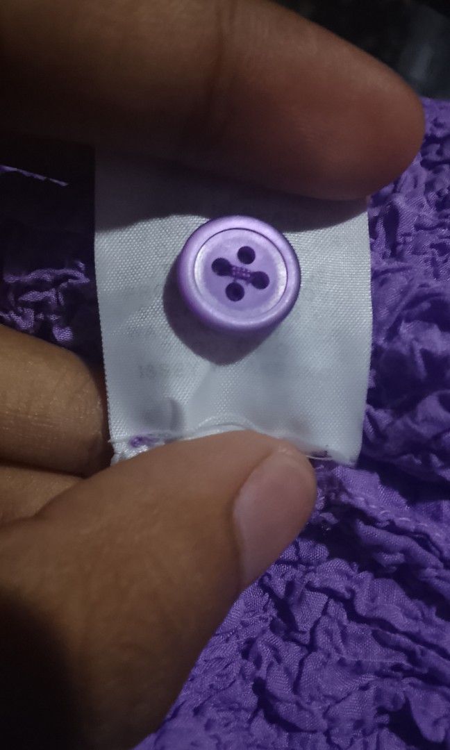 PLEATS ME (Category: Blouses) located in Manila. Submitted by plong7 (Listing ID 1468638541, Image 3). Description: Item Info Style: Textured crinkle-knit mock neck top Color: Bright purple / lavender Details: - Ruffled high mock neck with 2-button henley placket - Short cap sleeves with ruffled edges - All-over crinkled/textured fabric — stretchy, lightweight - Matching fabric flower appliqué on lower left side - Slim, body-conscious fit Fabric: