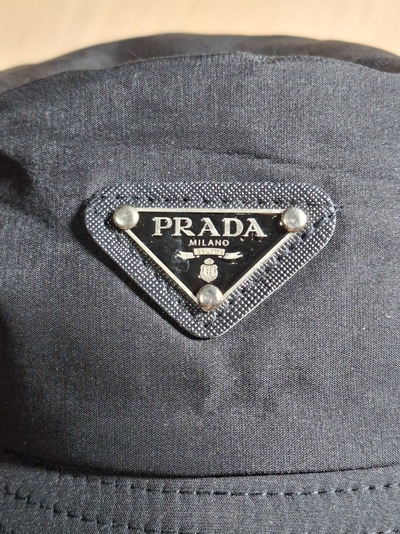 Prada Black Nylon Bucket Hat (Category: Caps & Hats) located in Baguio. Submitted by restyrille77846 (Listing ID 1468643779, Image 2). Description: - Color: Black - Material: Durable nylon - Details: Classic triangular metal logo plaque on the side, quilted stitching on the brim, and blue interior brand label - Condition: Clean surface with minimal signs of handling - Style: Great staple accessory for everyday outfits.
