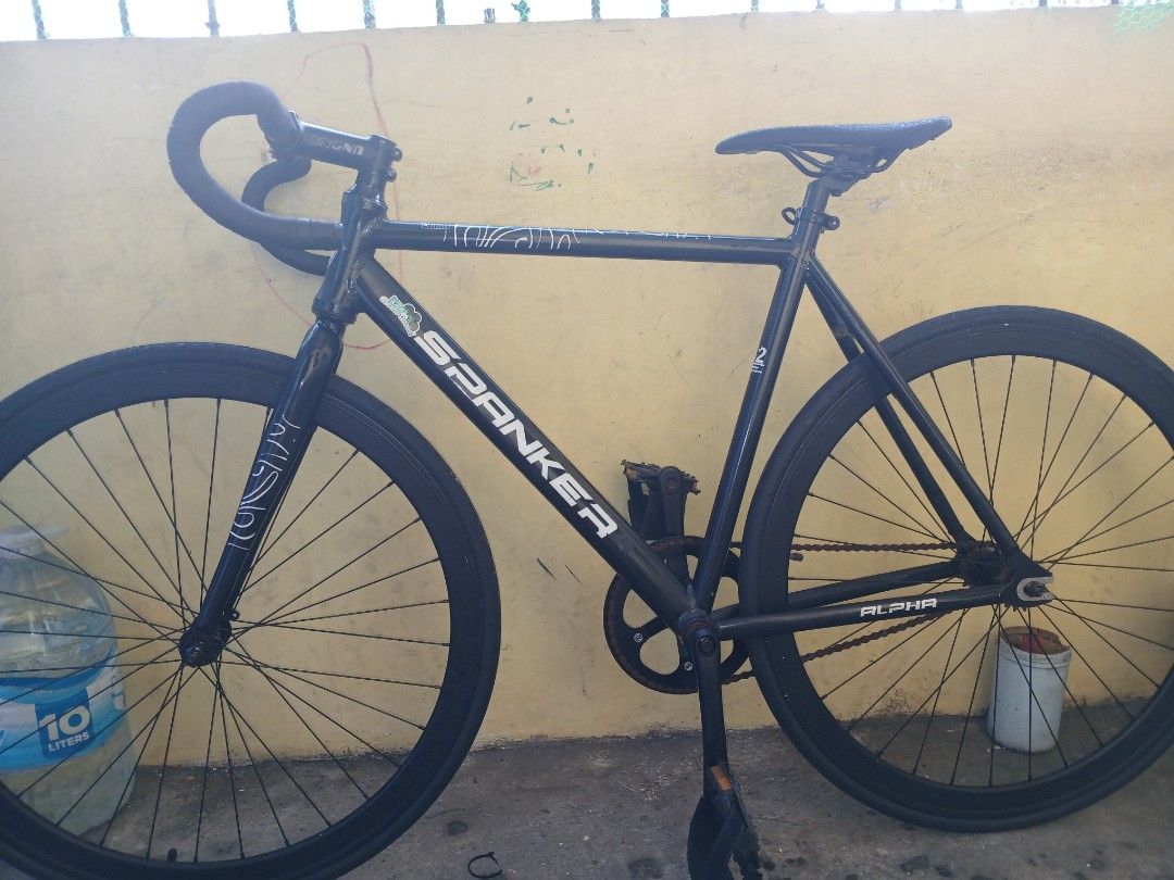 Spanker Alpha Fixie Bike Black (Category: Bicycles) located in Valenzuela. Submitted by prmontefalcon (Listing ID 1468514497, Image 3). Description: - Brand/Model: Spanker Alpha fixie bike - Color: Matte black with minor frame stickers - Handlebars: Bullhorn style (UNO) - Wheels: Deep dish rims (stock) - Saddle: Minimalist black (mosaic) - Drivetrain: Single-speed, fixed gear riding style (chain has some surface rust) - Condition: Solid frame geo