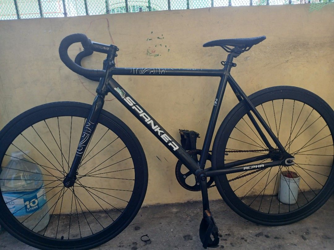 Spanker Alpha Fixie Bike Black (Category: Bicycles) located in Valenzuela. Submitted by prmontefalcon (Listing ID 1468514497, Image 2). Description: - Brand/Model: Spanker Alpha fixie bike - Color: Matte black with minor frame stickers - Handlebars: Bullhorn style (UNO) - Wheels: Deep dish rims (stock) - Saddle: Minimalist black (mosaic) - Drivetrain: Single-speed, fixed gear riding style (chain has some surface rust) - Condition: Solid frame geo