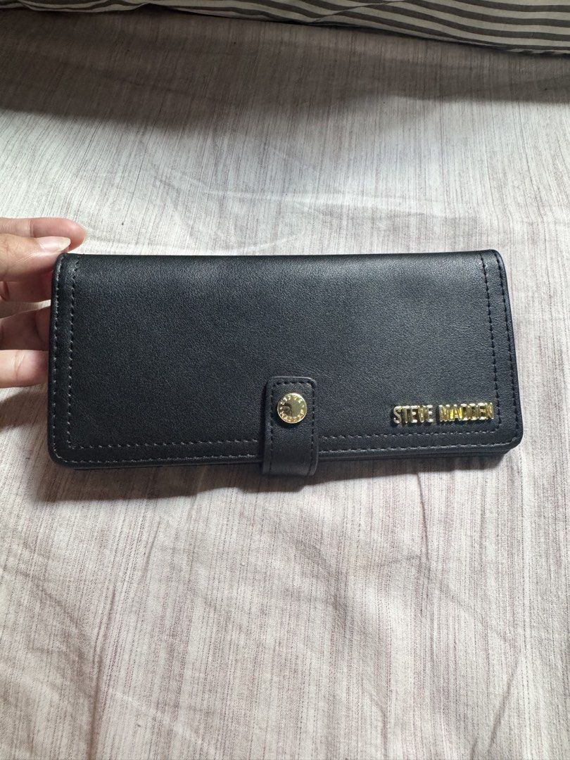 Steve Madden Black Long Wallet (Category: Wallets & Card holders) located in Las Pinas. Submitted by nautikath18 (Listing ID 1468552180, Image 1). Description: - Brand: Steve Madden - Color: Classic black with elegant gold-tone hardware - Closure: Secure front flap with snap button - Exterior: Convenient back zipper pocket - Interior: Multiple card slots and a clear ID window - Condition: Clean interior, very well-maintained, ideal for everyday u