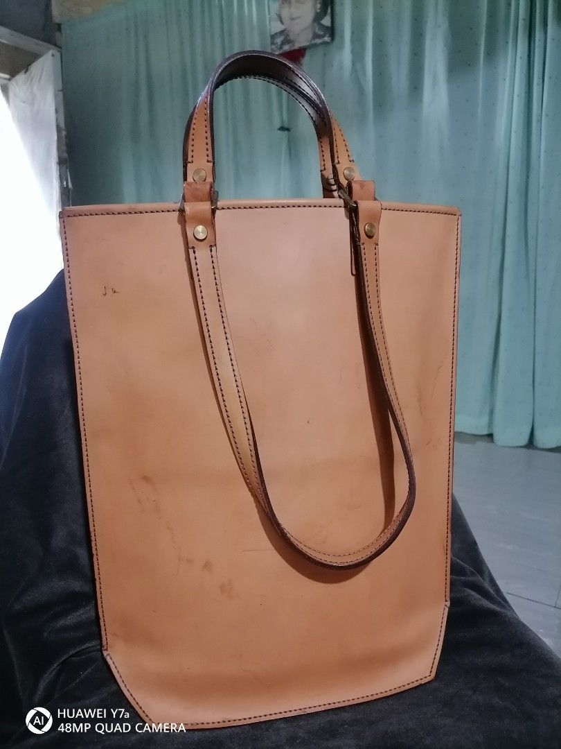 Tan Leather Tote Bag (Category: Tote Bags) located in Naga. Submitted by mrwisethrifter (Listing ID 1468515459, Image 2). Description: - Style: Tan leather tote bag with contrast stitching - Handles: Sturdy, structured double handles - Base: Flat hexagonal base that stands upright on surfaces - Storage: Interior zipper pocket for secure storage - Hardware: Brass finish - Condition: Visible scuffs, marks, and natural patina from previous use.