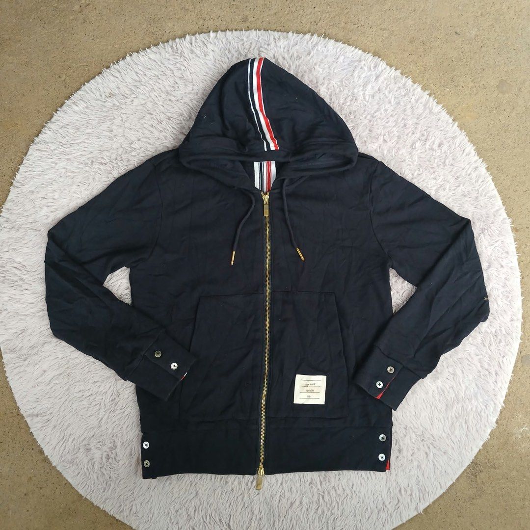 Thom Browne New York Hooded Zip Jacket (Category: Coats, Jackets and Outerwear) located in Montevista. Submitted by rdthriftshub (Listing ID 1468546876, Image 3). Description: - Brand: Thom Browne New York - Style: Full zip hoodie in dark navy - Material: 100% premium cotton - Details: Signature red, white, and blue grosgrain stripe tape on hood and inner collar - Hardware: Gold-tone dual zipper pulls - Features: Button cuffs, side hem vents with