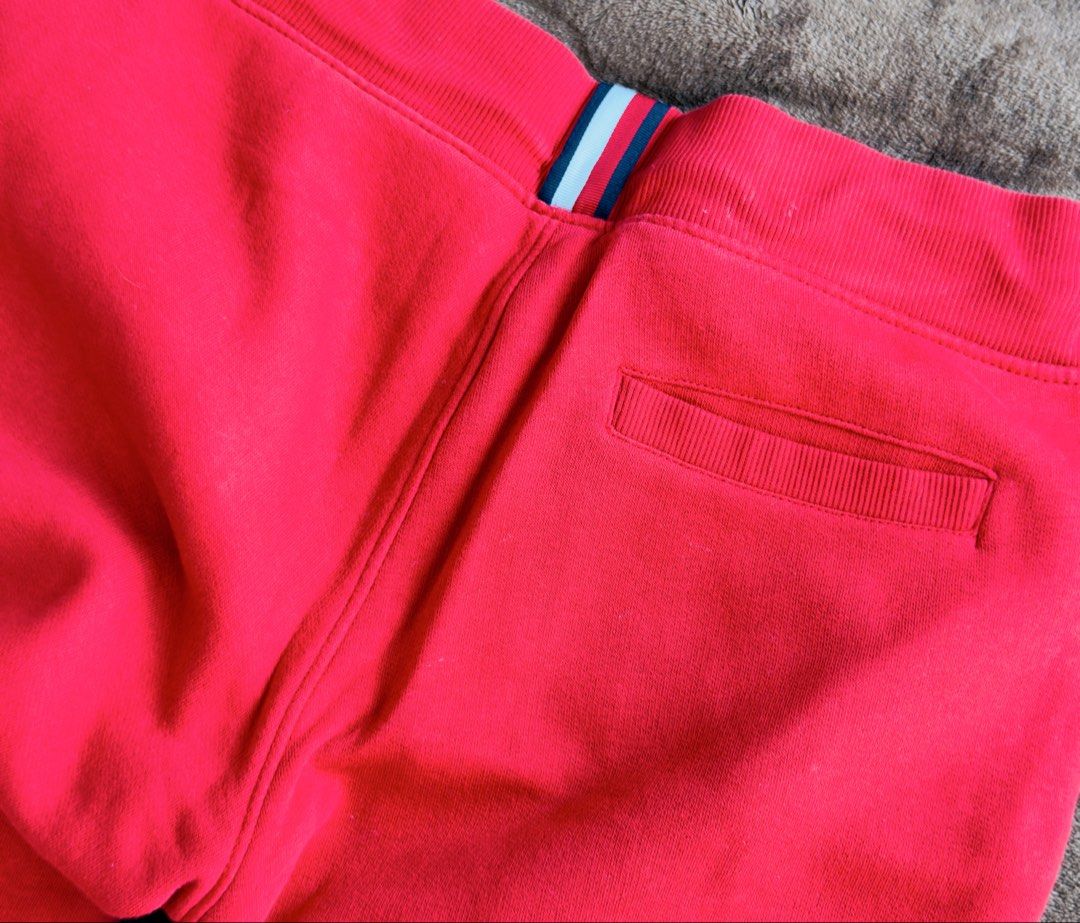 Tommy Hilfiger Red Sweatpants Size 152 (Category: Babies & Kids Fashion) located in Cainta. Submitted by sixteenfive29 (Listing ID 1468601664, Image 3). Description: - Brand: Tommy Hilfiger - Color: Bright red with large white logo on the right leg - Size: 152 - Features: Elastic waistband, striped drawstring with branded eyelets, and one back pocket with trim detail - Condition: Good, but has a small tear near the seam (refer to the last photo).