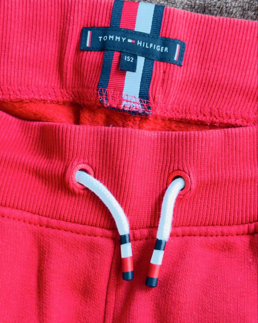 Tommy Hilfiger Red Sweatpants Size 152 (Category: Babies & Kids Fashion) located in Cainta. Submitted by sixteenfive29 (Listing ID 1468601664, Image 2). Description: - Brand: Tommy Hilfiger - Color: Bright red with large white logo on the right leg - Size: 152 - Features: Elastic waistband, striped drawstring with branded eyelets, and one back pocket with trim detail - Condition: Good, but has a small tear near the seam (refer to the last photo).