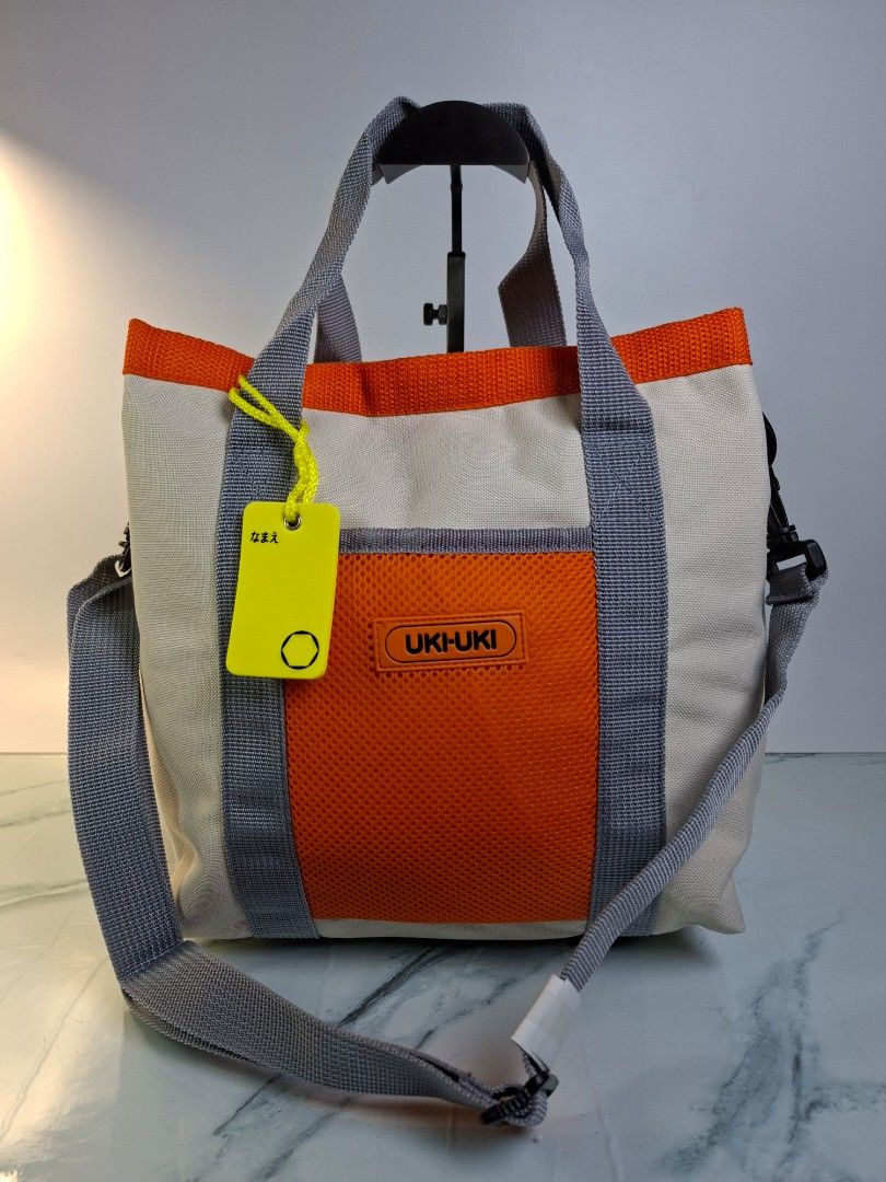UKI-UKI Canvas Tote Bag Orange and Grey (Category: Tote Bags) located in Pasay City. Submitted by onick_79 (Listing ID 1468694759, Image 1). Description: - Brand: UKI-UKI - Material: Sturdy canvas with crisp fabric and clean interior - Colorway: Cream body, bright orange trim, and grey webbing straps - Versatile Carry: Includes dual hand handles and an adjustable shoulder strap with black hardware - Extra Storage: Front orange mesh pocket with a 