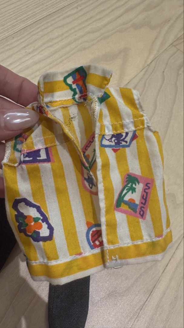 Vintage ken Doll vest (Category: Sleeveless) located in Mandaluyong City. Submitted by maelovestoshop (Listing ID 1468689689, Image 2). Description: - Item: Doll outfit (Vest and Denim Pants) - Top: Yellow and white striped vest with colorful tropical graphics and travel stamp motifs - Bottoms: Matching dark blue denim pants - Fit: Standard fashion dolls - Condition: Good, with minor age spots and discoloration on the vest collar/shoulder (see cl