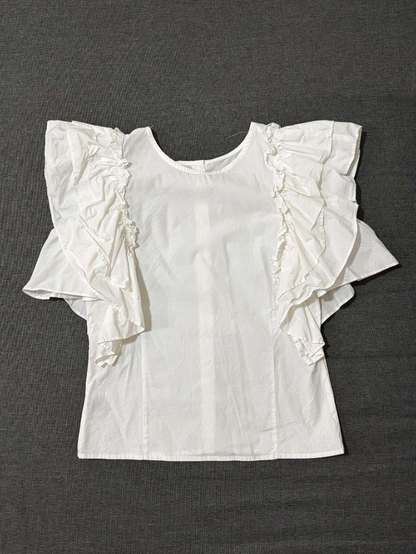 White Ruffle Sleeve Blouse with Button-Up Back (Category: Blouses) located in Lipa City. Submitted by xandibaronix (Listing ID 1468687480, Image 2). Description: - Color/Material: White cotton, lightweight and breezy - Design: Dramatic layered ruffle sleeves with button-up closure at the back - Condition: Pre-loved with small stains (fixable with a quick wash or spot clean) - Style Tip: Pair with jeans or a skirt for a chic, effortless look! - Ca
