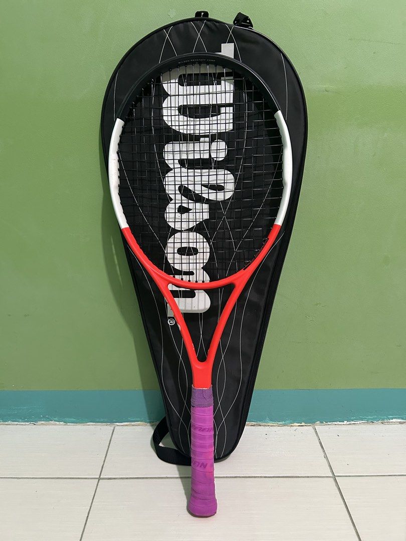 Wilson Pro Staff Comp Tennis Racket with Cover (Category: Racket and Ball Sports) located in Imus. Submitted by storiesforstrays (Listing ID 1468638718, Image 1). Description: Wilson Pro Staff Comp tennis racket. Orange, white, and black colorway. Strung and ready to play. Includes the original Wilson black racket cover bag with zip closure. Frame is clean with minimal scuffs. .