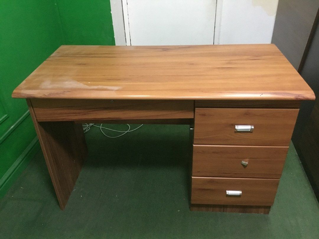 Wooden office desk with storage drawers (Category: Office Furniture & Fixtures) located in Manila. Submitted by roberto.enriquez (Listing ID 1468689864, Image 2). Description: - Material & Finish: Solid wooden study desk in a warm brown tone with sturdy panel legs - Storage: 1 wide keyboard/shallow top drawer and 3 stacked side drawers with sleek silver pull handles - Condition: Good overall condition with a minor lighter wear mark on the left si