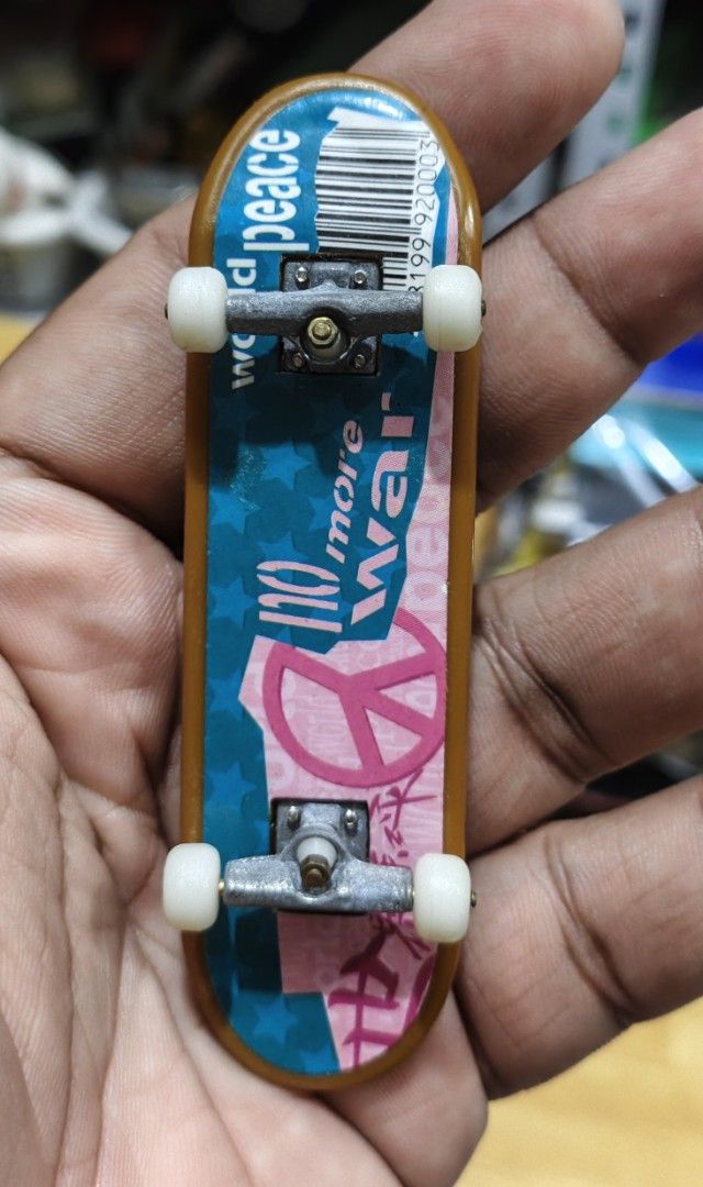 World Peace Fingerboard Mini Skateboard (Category: Skates, Rollerblades & Scooters) located in San Pedro. Submitted by toydibz (Listing ID 1468538375, Image 2). Description: - Type: Standard tech deck style fingerboard - Bottom Design: World Peace graphic with blue stars and a pink peace sign - Top Grip: Black grip tape featuring white 'Sk@te' and barcode print - Hardware: White wheels and metal trucks attached - Use: Fun little toy perfect for y