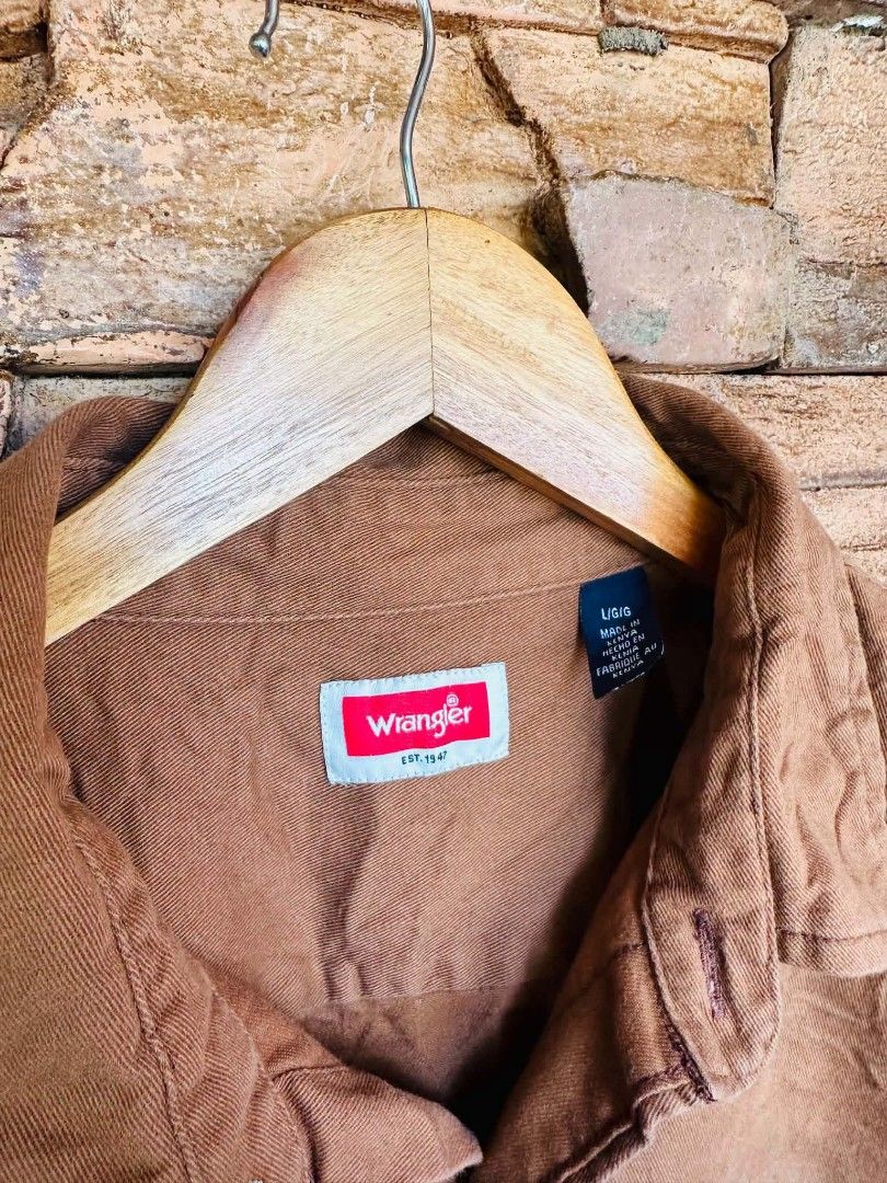 Wrangler Brown Long Sleeve Button Down Shirt Size L (Category: Coats, Jackets and Outerwear) located in Santiago. Submitted by reyibanez253969 (Listing ID 1468631641, Image 2). Description: - Brand: Wrangler - Style: Long sleeve button-down utility shirt - Color: Solid brown - Size: L (Regular fit) - 23.5x29 - Features: Classic collar, 2 chest pockets with button flaps, branded buttons, and signature red logo tags on hem and inner cuff - Origin: 