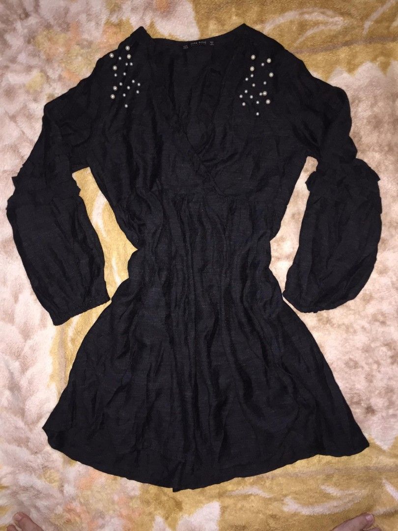 ZARA Basic Black Flowy Mini Dress (Category: Dresses) located in Dasmarinas. Submitted by pepperronnie (Listing ID 1468584789, Image 1). Description: This is a Zara Basic black flowy mini dress with pearl details 🖤 Style Breakdown: - Silhouette: Wrap V-neck, empire waist, A-line mini skirt — very flattering & forgiving fit ​ - Sleeves: Billowy balloon sleeves with ruffled cuffs — romantic, boho vibe ​ - Details: Faux pearl embellishments at shou