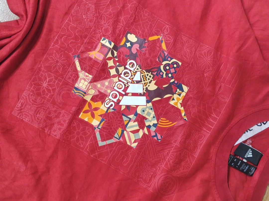 Adidas Red Graphic T-Shirt (Category: Tshirts & Polo Shirts ) located in Manila. Submitted by dp.finds (Listing ID 1468919818, Image 3). Description: - Brand: Adidas - Color: Red with colorful graphic - Size: Asia A/XL (170/96A) - Design: Snowflake and logo graphic with subtle geometric pattern on a square front panel - Features: Short sleeves, crew neck - Condition: Inventory sticker attached to the inside collar label.