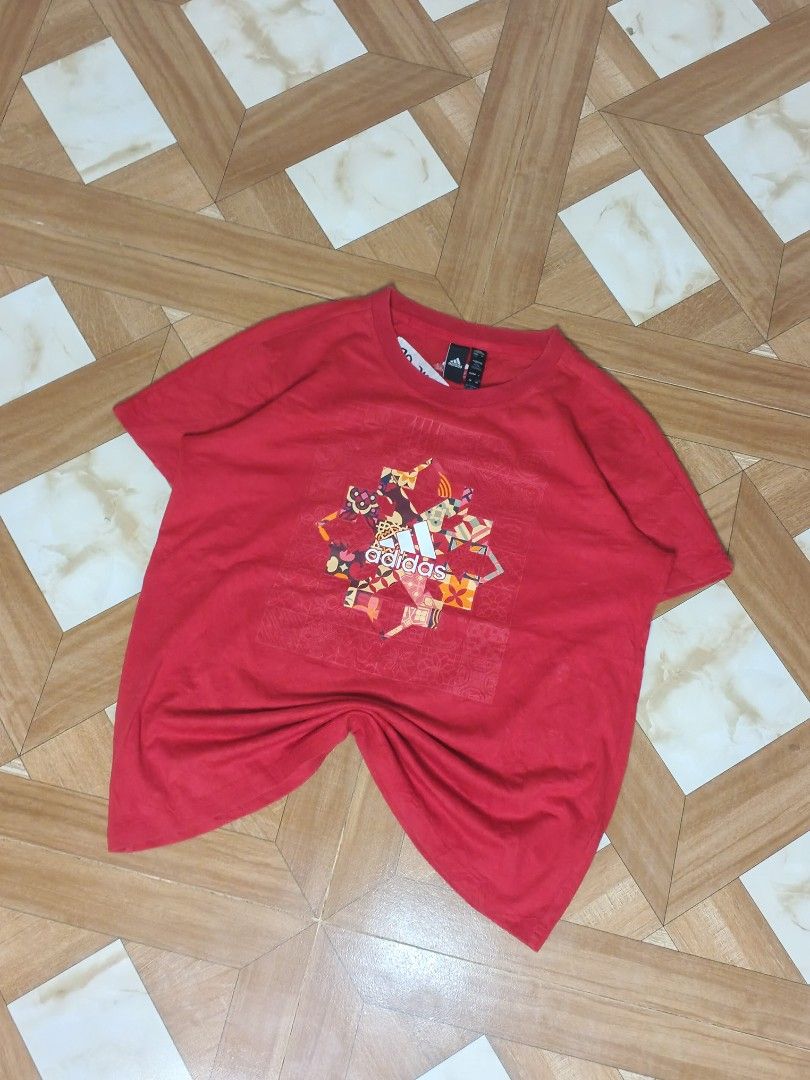 Adidas Red Graphic T-Shirt (Category: Tshirts & Polo Shirts ) located in Manila. Submitted by dp.finds (Listing ID 1468919818, Image 2). Description: - Brand: Adidas - Color: Red with colorful graphic - Size: Asia A/XL (170/96A) - Design: Snowflake and logo graphic with subtle geometric pattern on a square front panel - Features: Short sleeves, crew neck - Condition: Inventory sticker attached to the inside collar label.