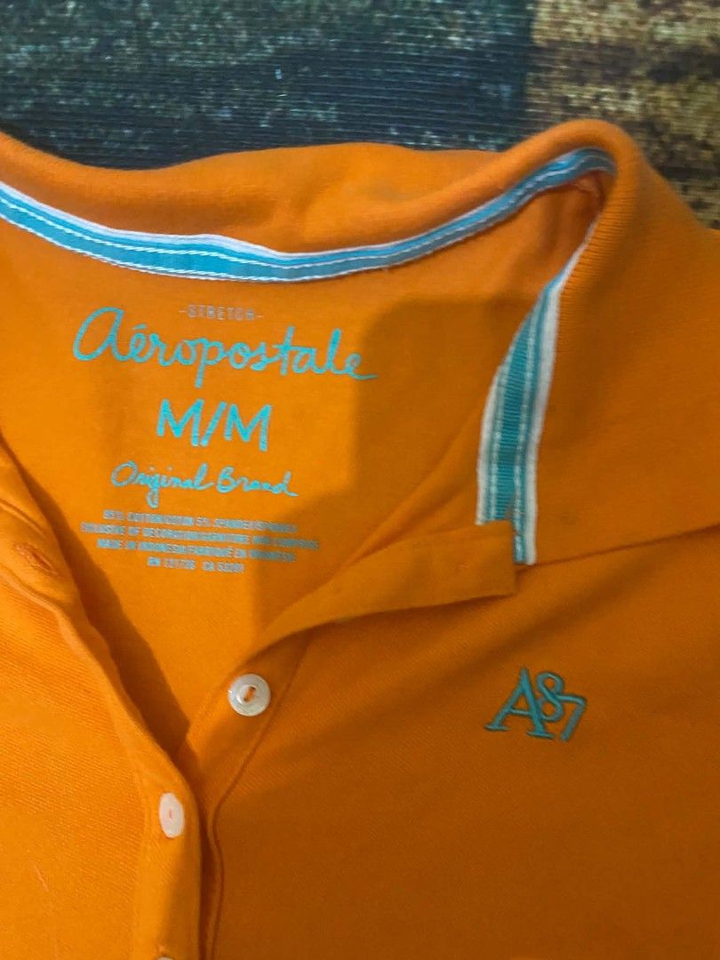 Aeropostale Orange Stretch Polo Shirt (Category: Shirts) located in Quezon City. Submitted by andreialej28522 (Listing ID 1468720302, Image 2). Description: - Brand: Aeropostale - Size: Medium (M) - Color: Bright orange with turquoise blue details - Material: 95% Cotton, 5% Spandex (stretch fit) - Design: Short sleeves, 3-button placket, contrast collar lining, and AS87 chest embroidery - Condition: Excellent pre-loved condition, smoke-free home.