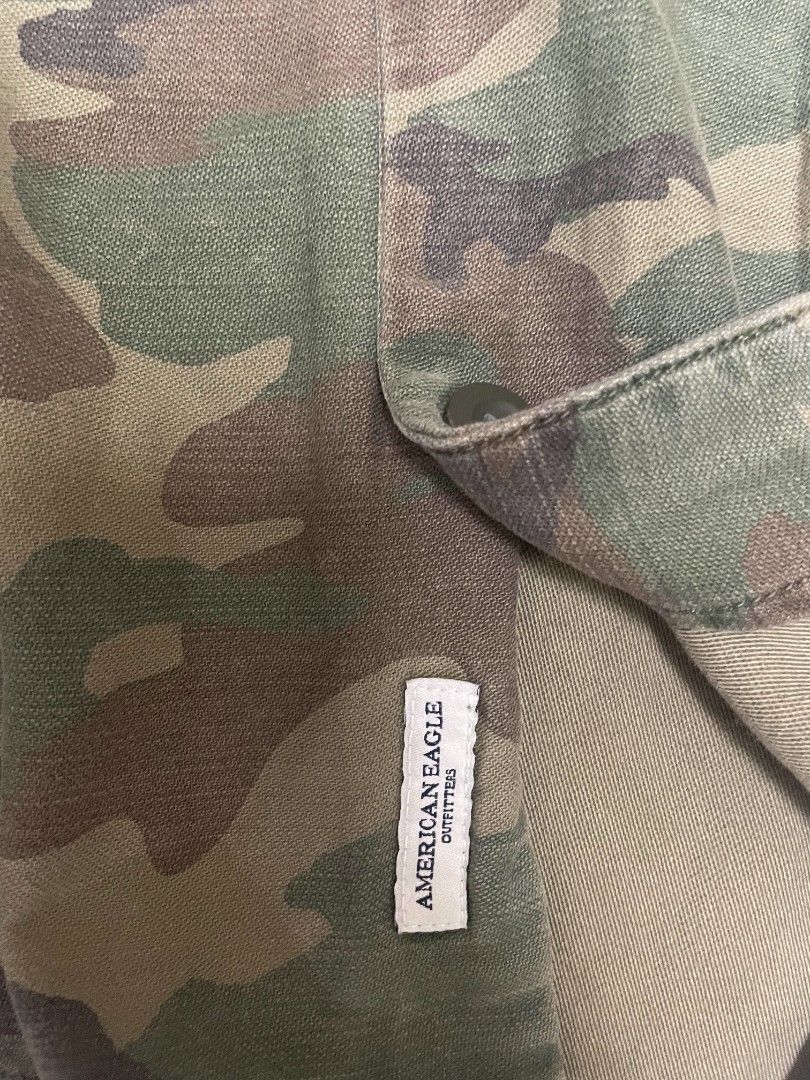 American Eagle longsleeve polo camo (Category: Coats, Jackets and Outerwear) located in Lipa City. Submitted by t1pce3garmentz (Listing ID 1468729719, Image 3). Description: - Brand: American Eagle Outfitters - Size: XL (TG/EXG) - Print: Classic green and brown camouflage - Features: Button-down front, structured collar, two front chest pockets, and button cuffs - Material: Heavy-duty fabric construction - Condition: Clean interior with original 