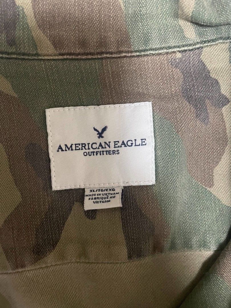 American Eagle longsleeve polo camo (Category: Coats, Jackets and Outerwear) located in Lipa City. Submitted by t1pce3garmentz (Listing ID 1468729719, Image 2). Description: - Brand: American Eagle Outfitters - Size: XL (TG/EXG) - Print: Classic green and brown camouflage - Features: Button-down front, structured collar, two front chest pockets, and button cuffs - Material: Heavy-duty fabric construction - Condition: Clean interior with original 