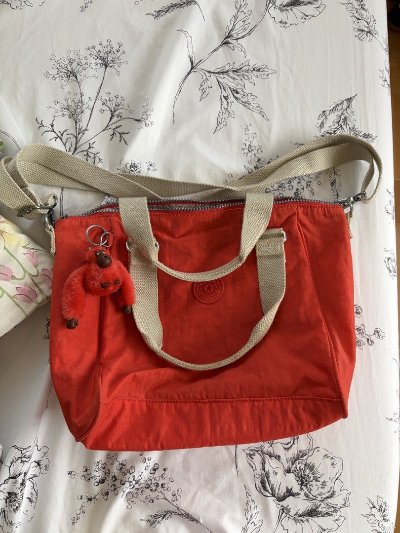 Authentic Kipling Red/Orange Tote Bag with Crossbody Strap (Category: Tote Bags) located in Bulacan. Submitted by fallongallon (Listing ID 1468734455, Image 1). Description: - Vibrant orange Kipling tote bag with stylish beige top handles - Includes an adjustable shoulder strap and the signature fuzzy monkey keychain - Secure zip-top closure for peace of mind - Spacious interior featuring patterned grey lining, a zippered pocket, and slip compart