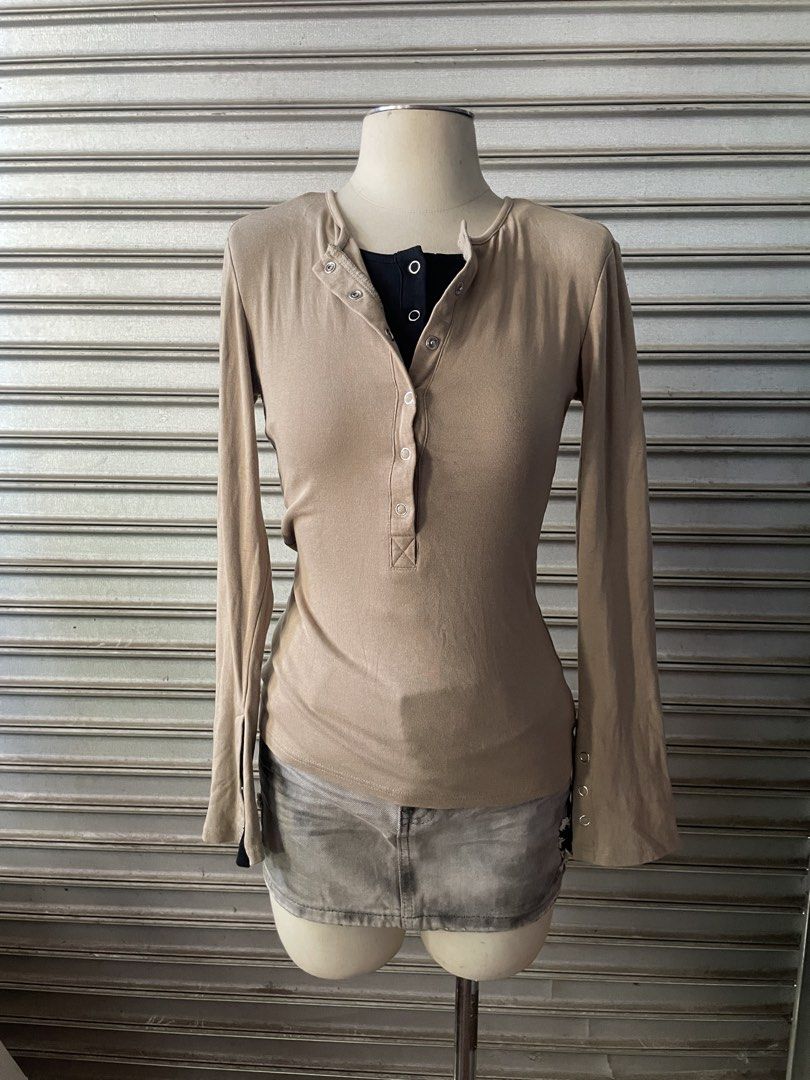 Beige Long Sleeve Henley Top with Contrast Black Layer (Category: Longsleeves) located in Davao. Submitted by riab_qt (Listing ID 1468777919, Image 1). Description: - Color: Beige with black layered inner collar and cuffs - Neckline: Henley style with silver snap buttons - Sleeves: Long flared sleeves with wrist button details - Material: Soft and stretchy ribbed fabric - Fit: Fitted cut that hugs the body - Styling tip: Looks amazing paired with