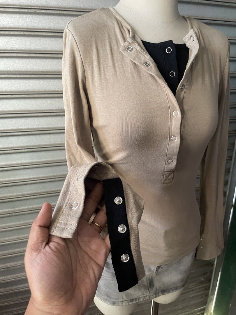 Beige Long Sleeve Henley Top with Contrast Black Layer (Category: Longsleeves) located in Davao. Submitted by riab_qt (Listing ID 1468777919, Image 3). Description: - Color: Beige with black layered inner collar and cuffs - Neckline: Henley style with silver snap buttons - Sleeves: Long flared sleeves with wrist button details - Material: Soft and stretchy ribbed fabric - Fit: Fitted cut that hugs the body - Styling tip: Looks amazing paired with