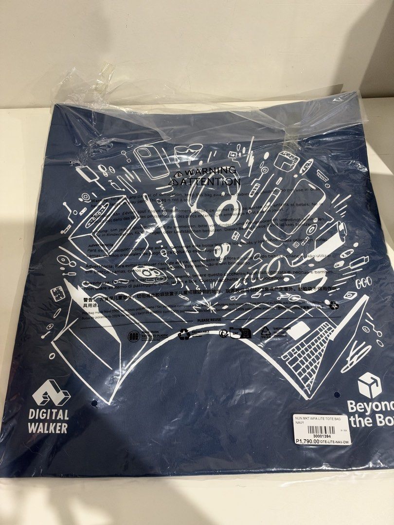 Beyond the Box x Digital Walker WFA Lite Tote Bag (Category: Tote Bags) located in Marilao. Submitted by angelica10 (Listing ID 1468729313, Image 1). Description: - Brand: Beyond the Box x Digital Walker collaboration - Color: Navy blue with white tech-themed line art graphic (laptops, headphones, phones) - Condition: Brand new, still sealed in original plastic packaging with barcode and retail price tag - Features: Standard flat tote handles, du