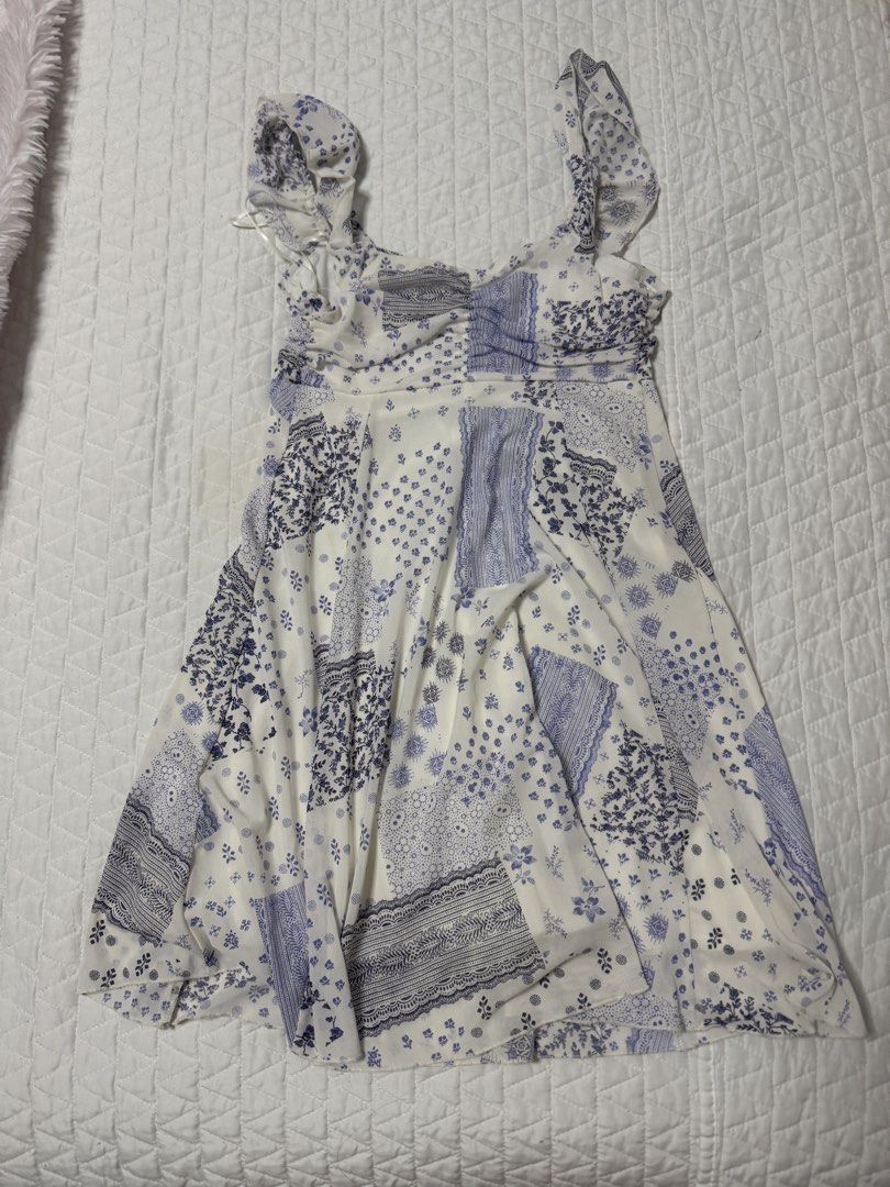 Blue and White Patchwork Print Ruffle Strap Dress (Category: Dresses) located in Manila. Submitted by mattigarciaa (Listing ID 1468775411, Image 1). Description: - Design: Blue and white patchwork pattern with charming floral and lace motifs - Neckline & Straps: Square neckline with playful ruffled shoulder straps - Fit: Gathered bust detail and a flattering flared skirt - Fabric: Lightweight and breathable, ideal for sunny, warm weather - Condit
