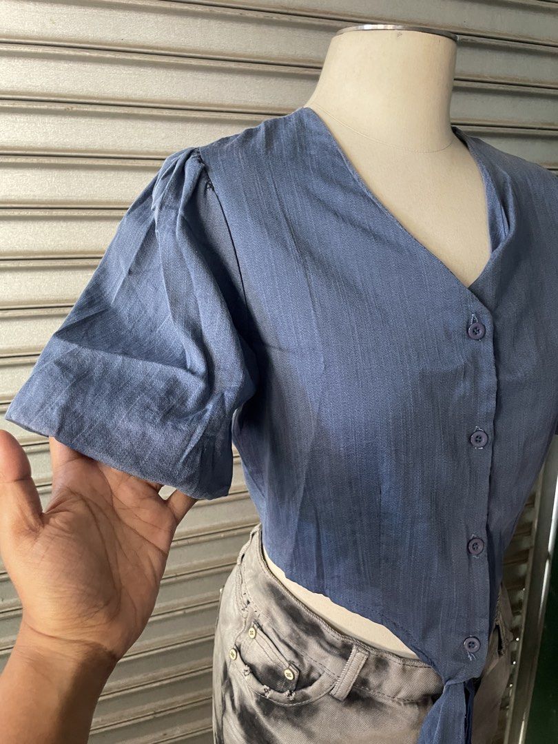Blue Button-Up Tie Front Short Sleeve Crop Top (Category: Blouses) located in Davao. Submitted by riab_qt (Listing ID 1468776005, Image 2). Description: - Color: Blue - Style: Short sleeve crop top with V-neckline and button-down front - Details: Puffy shoulders and trendy self-tie hem - Fabric: Lightweight and textured, very comfortable - Perfect Match: Looks great with high-waisted shorts or skirts - Condition: Brand new / Excellent.