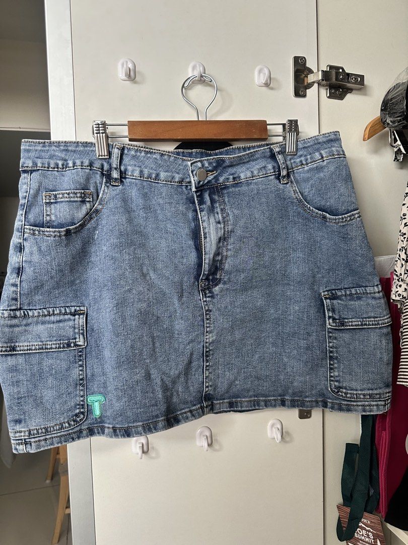 Blue Denim Cargo Skirt with Side Pockets Size M (Category: Skirts) located in Caloocan City. Submitted by be.iiiii (Listing ID 1468828947, Image 1). Description: - Style: Medium wash denim cargo skirt - Details: Front zip and button closure, belt loops, and panel stitching on the back - Pockets: Functional utility side pockets on both hips - Accent: Small turquoise embroidered logo near the bottom left hem - Fit: Classic mid-rise - Pairing: Great