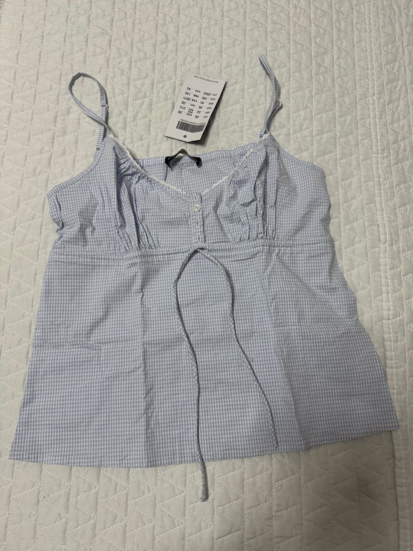 Brandy Melville Blue Gingham Camisole Top (Category: Sleeveless) located in Manila. Submitted by mattigarciaa (Listing ID 1468877589, Image 1). Description: - Brand: Brandy Melville (Original store tag still attached) - Color: Light blue and white gingham - Design: Thin adjustable spaghetti straps, gathered bust with white button, and delicate white lace trim - Detail: Cute tie closure right under the bust line - Condition: Brand new, never worn 