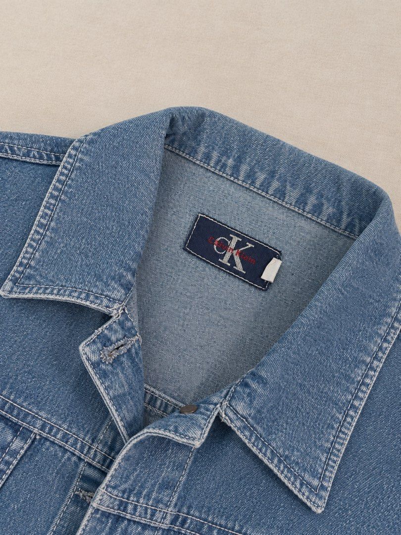Calvin Klein Blue Denim Jacket (Category: Coats, Jackets and Outerwear) located in Manila. Submitted by lexiandco.ph (Listing ID 1468722141, Image 1). Description: - Brand: Calvin Klein - Color: Classic Blue - Material: Durable denim - Features: Metal front button closure, two chest flap pockets, button cuffs, and structured collar - Details: Contrast stitching throughout - Fit: Easy layering piece for cooler weather - Condition: Pre-loved, well-