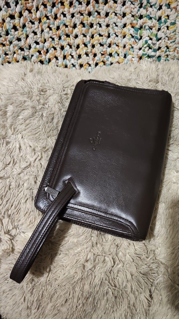 Capacci brown leather clutch bag with wrist strap (Category: Clutches) located in Cebu City. Submitted by lumaynojes00490 (Listing ID 1468803188, Image 3). Description: - Brand: Capacci - Color: Deep dark brown with a polished finish - Material: Premium leather with structured rectangular shape - Hardware: Silver-toned with smooth top zipper closure - Features: Attached side wrist strap and embossed front logo.