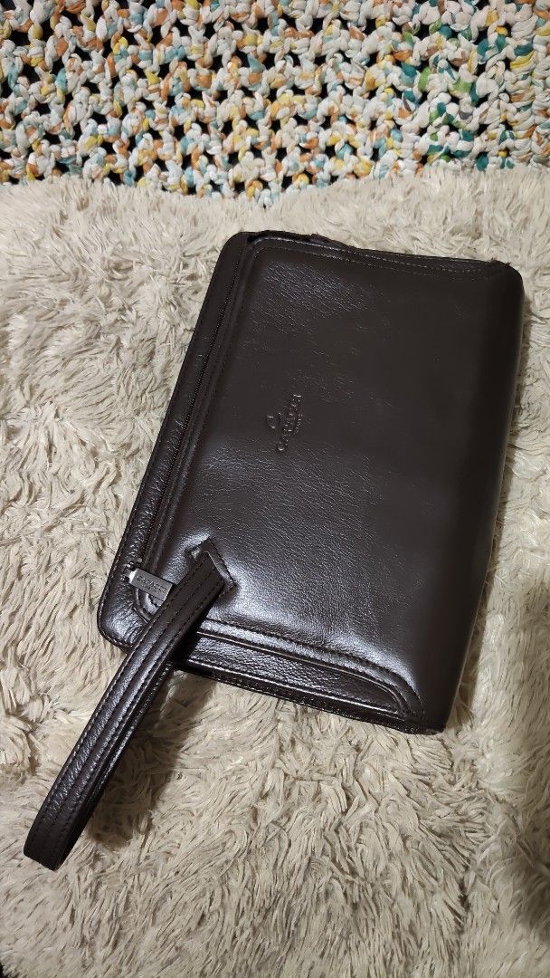 Capacci brown leather clutch bag with wrist strap (Category: Clutches) located in Cebu City. Submitted by lumaynojes00490 (Listing ID 1468803188, Image 1). Description: - Brand: Capacci - Color: Deep dark brown with a polished finish - Material: Premium leather with structured rectangular shape - Hardware: Silver-toned with smooth top zipper closure - Features: Attached side wrist strap and embossed front logo.