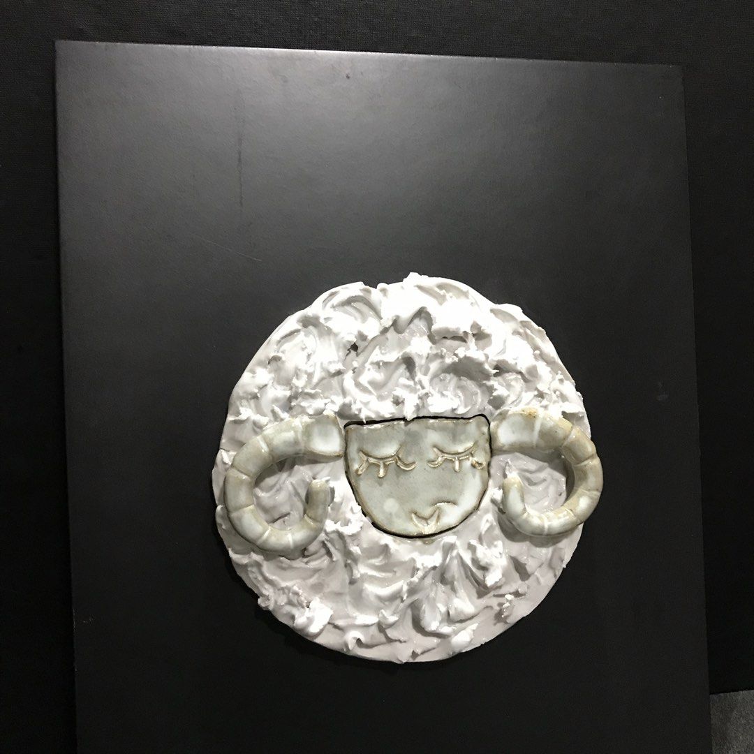 Ceramic sheep wall art sculpture mounted on black board (Category: Wall Decor) located in Baao. Submitted by all.things.japan (Listing ID 1468747832, Image 3). Description: 13.5 x 10.25 inches - Handmade ceramic sleeping sheep sculpture - Features textured white wool and curled horns - Securely mounted on a rectangular black board with a blue hanging cord - Unique art piece, perfect for home decor - Excellent, clean condition ready for display.