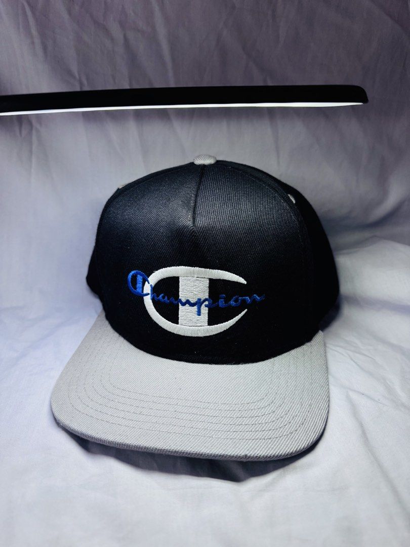 Champion x Supreme Snapback Cap Black Grey (Category: Caps & Hats) located in Roxas City. Submitted by patsquarephantz (Listing ID 1468857687, Image 2). Description: - Brand: Supreme x Champion - Color: Black and grey - Details: White/blue embroidered Champion logo on front, Supreme lettering on back - Fit: Adjustable plastic strap at the rear - Style: Structured crown with a flat brim - Condition: Clean stitching, solid construction.