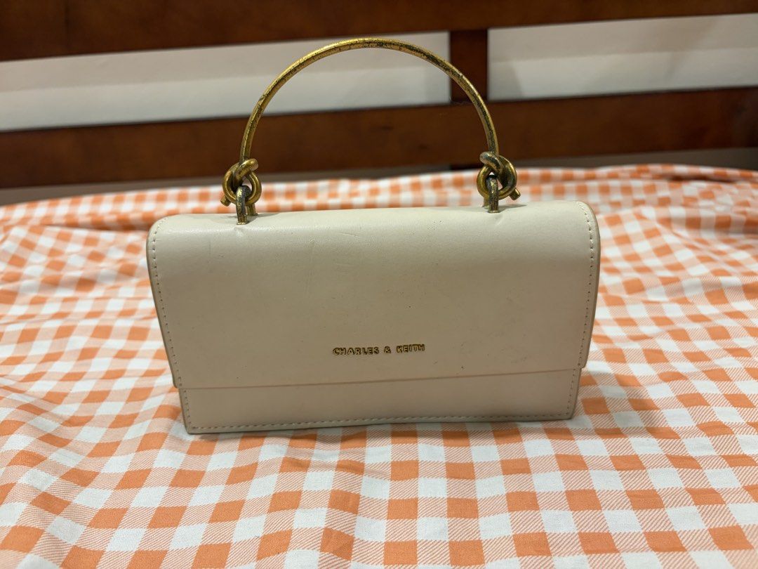 Charles & Keith Off-White Shoulder Bag (Category: Shoulder Bags) located in Manila. Submitted by jdace (Listing ID 1468844815, Image 2). Description: Charles & Keith shoulder bag in off-white faux leather. Gold-tone metallic top handle with slight tarnish near the knots. Flap closure with metallic branding on the front. Some surface scratches and scuffs on the leather body, mostly visible on the front flap. Clean interior structure..